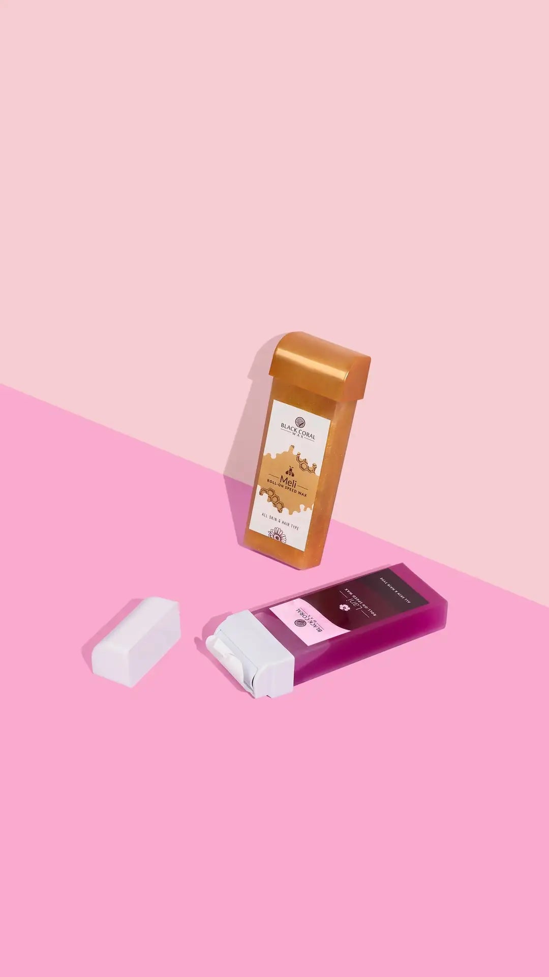 Two cosmetic containers on a pink background: an upright, rectangular, orange-brown container with a white label—ideal for honey wax—and a purple and white Meli Roll-On SpeedWax by Black Coral Wax USA lying down with its cap off for gentle waxing.