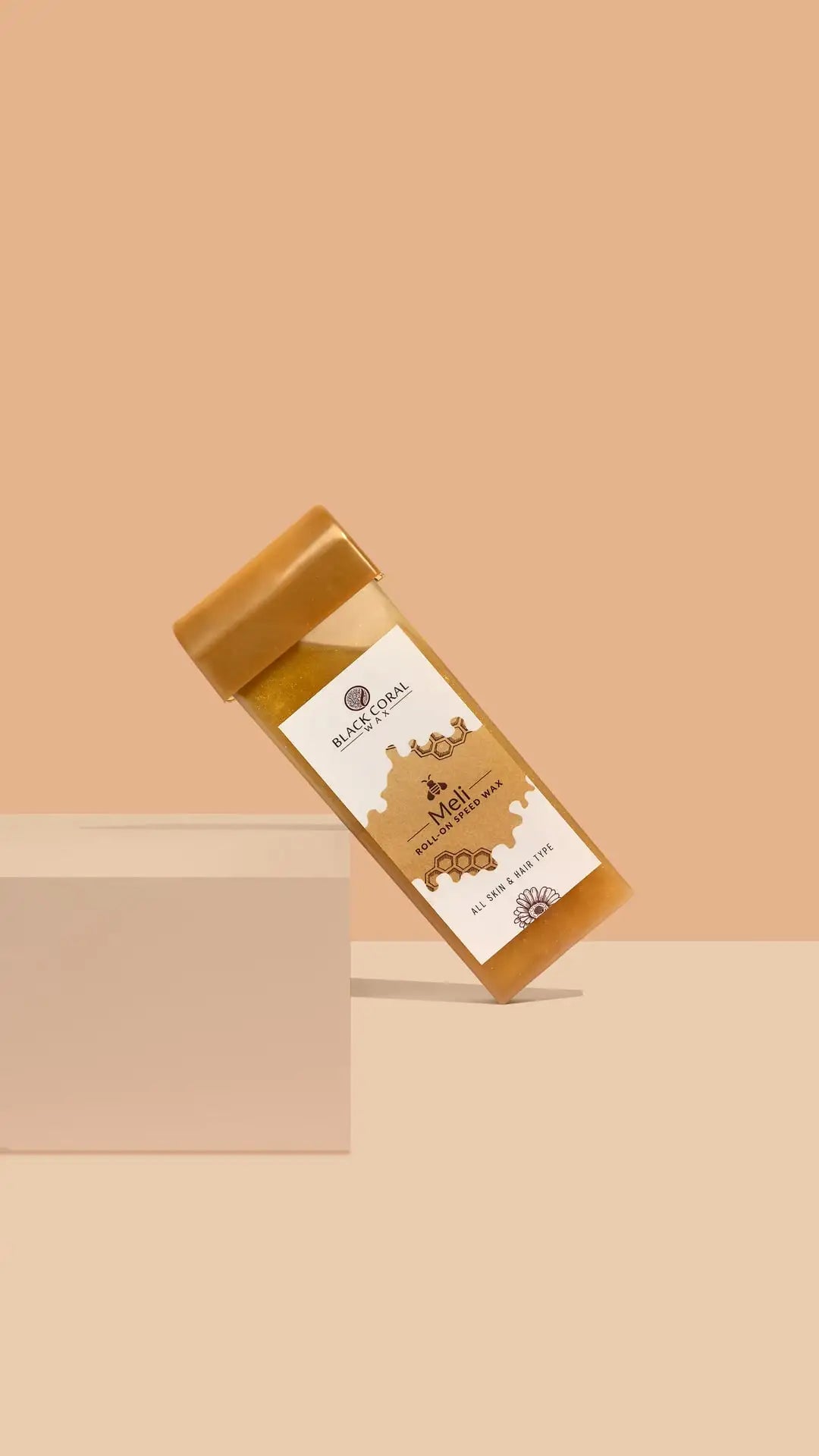 The Meli Roll-On SpeedWax by Black Coral Wax USA, in a rectangular honey-tone container with a golden cap and graphic label, leans against a white block on beige. The label highlights its gentle waxing formula.