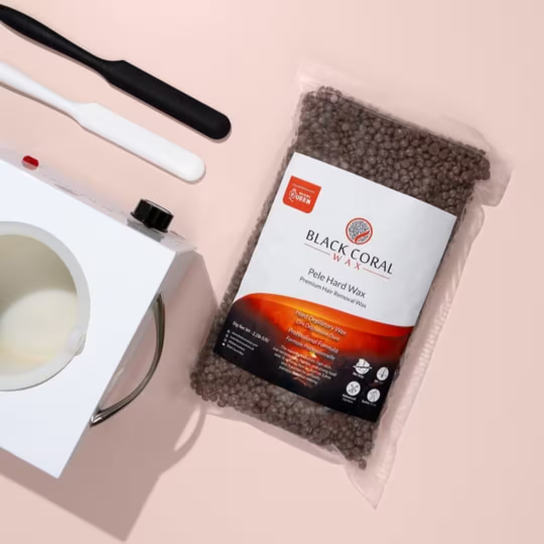 A bag of Pele Hard Wax Beads by Black Coral Wax USA sits next to a white wax warmer and two spatulas on a light beige surface—ideal for easily removing coarse hair.