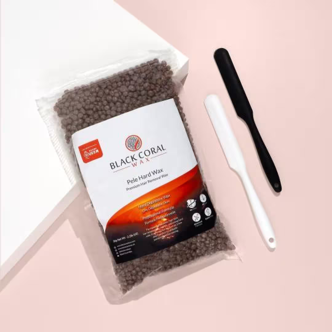 A bag of Pele Hard Wax Beads by Black Coral Wax USA for coarse hair rests on a light pink surface beside a black and a white waxing spatula.