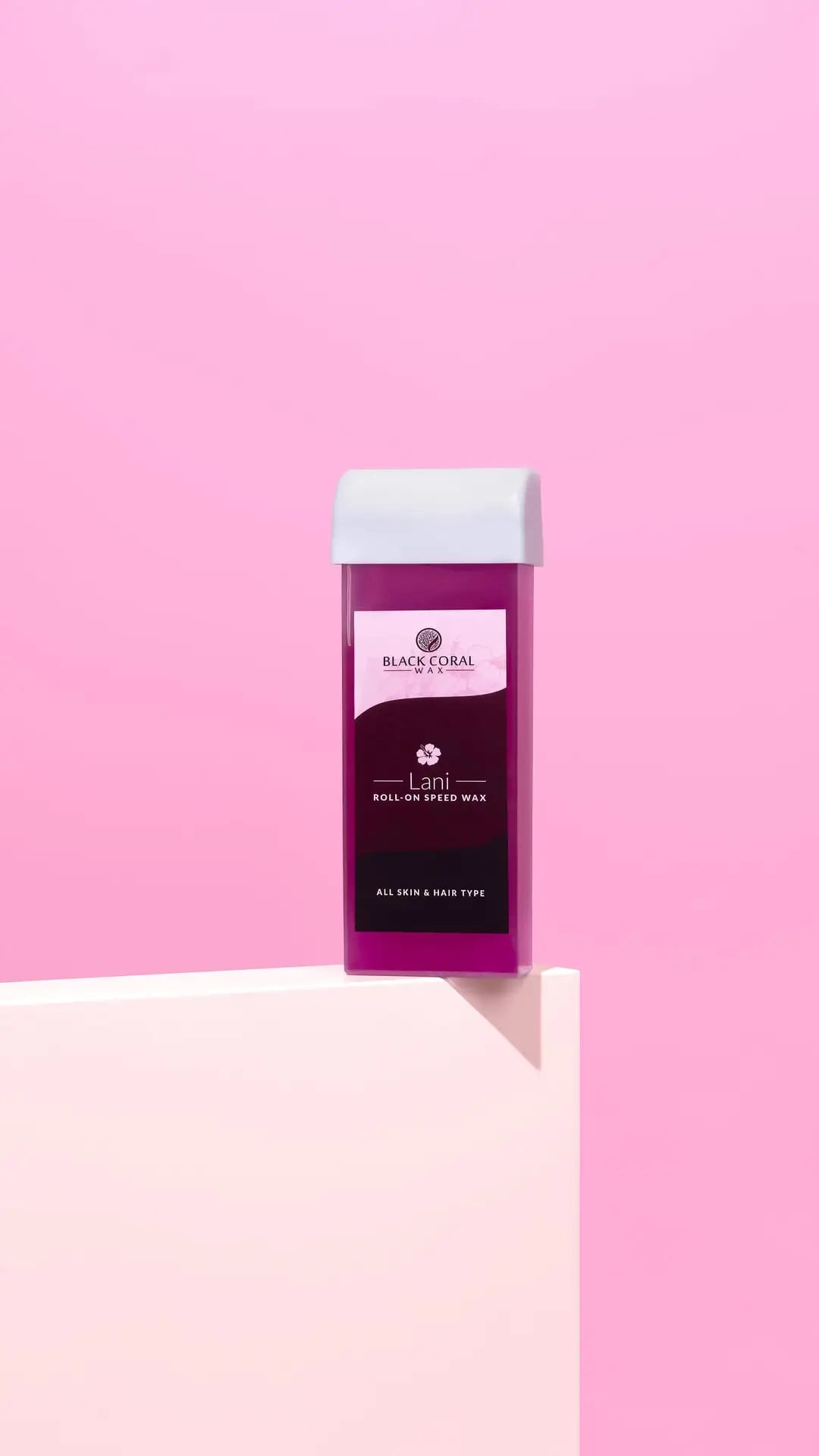 A rectangular roll-on wax cartridge with a purple label and white cap stands on a pastel pink surface against a solid pink background. The label reads Black Coral Wax USA Lani Roll-On SpeedWax, featuring gentle wax for smooth results.
