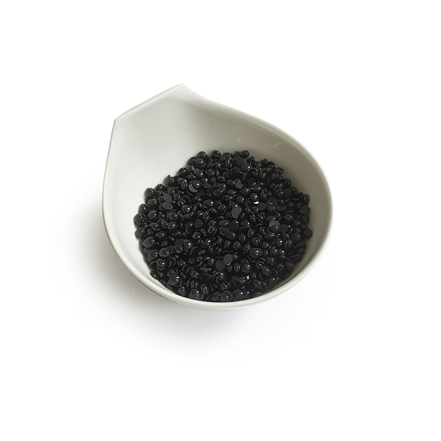 Black Coral Hard Wax by Black Coral Wax USA is showcased in a white ceramic bowl akin to a Black Coral Hard Wax vessel. The bowls subtle, spout-like design elegantly cradles small, shiny black beads against a plain backdrop, reflecting potential for long-lasting hair removal.