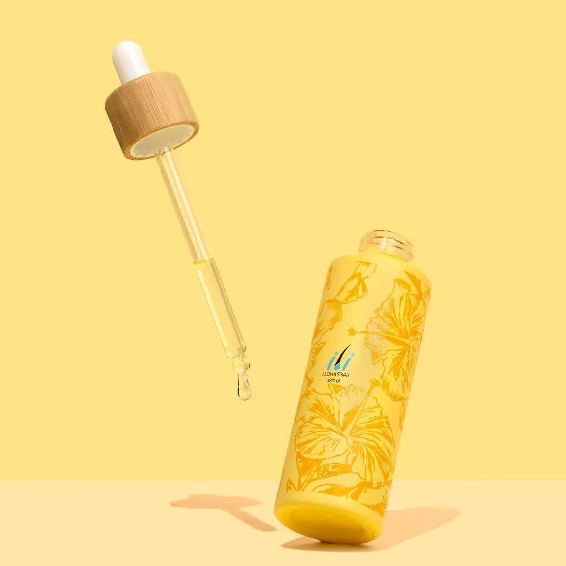 A 60ml yellow bottle of ili Oil by Black Coral Wax USA with floral designs stands upright beside a wooden dropper against a matching yellow background, highlighting its soothing, skin-moisturizing post-waxing formula.