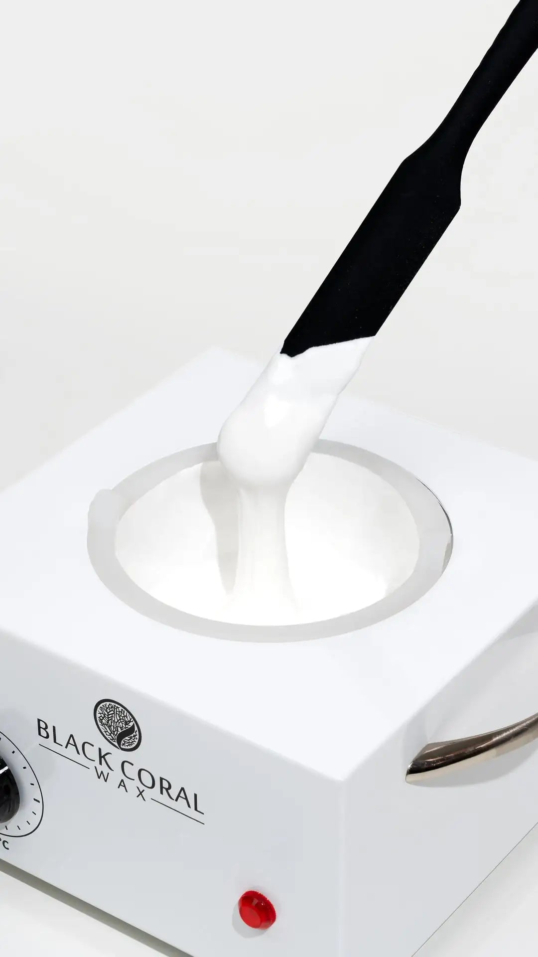 A black spatula lifts creamy White Coral Wax for hair removal from a white Black Coral Wax USA warmer, with smooth, stretchy wax—ideal for sensitive skin.