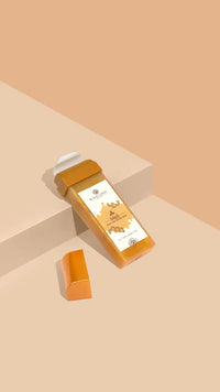 A rectangular Meli Roll-On SpeedWax by Black Coral Wax USA with a white cap and honeycomb label rests on a beige surface beside its orange cap, set against a peach background—ideal for gentle waxing.
