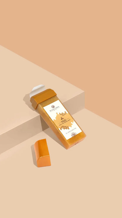 A rectangular Meli Roll-On SpeedWax by Black Coral Wax USA with a white cap and honeycomb label rests on a beige surface beside its orange cap, set against a peach background—ideal for gentle waxing.