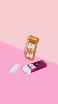 Two cosmetic containers on a pink and light pink background: one upright with a tan cap and label, the other—a Lani Roll-On SpeedWax cartridge by Black Coral Wax USA in purple and white—lying down with its cap off.