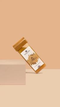 The Meli Roll-On SpeedWax by Black Coral Wax USA, in a rectangular honey-tone container with a golden cap and graphic label, leans against a white block on beige. The label highlights its gentle waxing formula.
