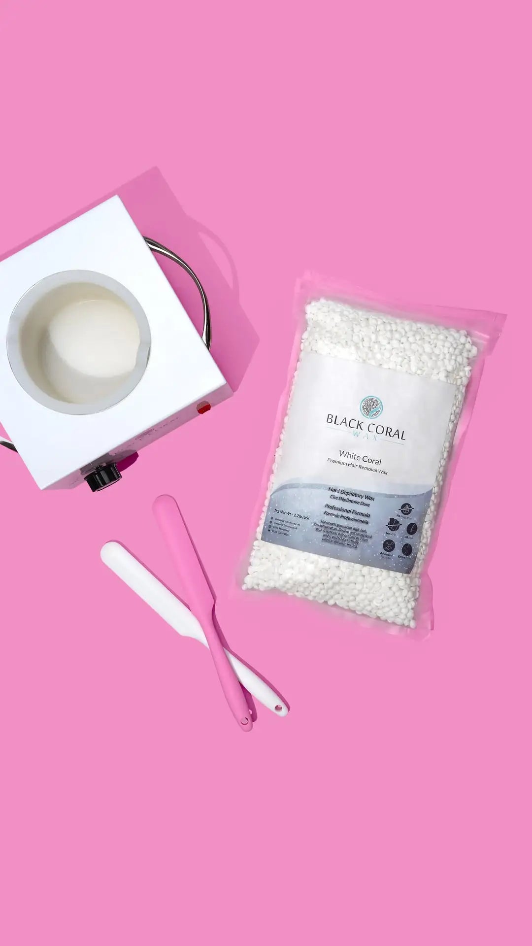 The White Coral Wax by Black Coral Wax USA, with hard wax beads for sensitive skin and two pink spatulas, is arranged on a bright pink background—perfect for gentle at-home hair removal.
