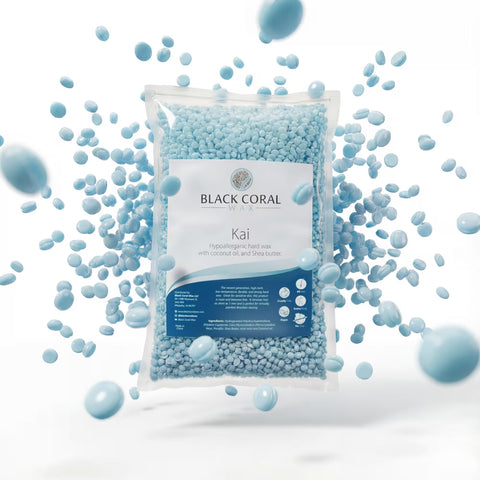 A bag of Kai Hard Wax by Black Coral Wax USA is surrounded by scattered blue beads in mid-air. The label highlights it as hypoallergenic, with coconut oil and shea butter.