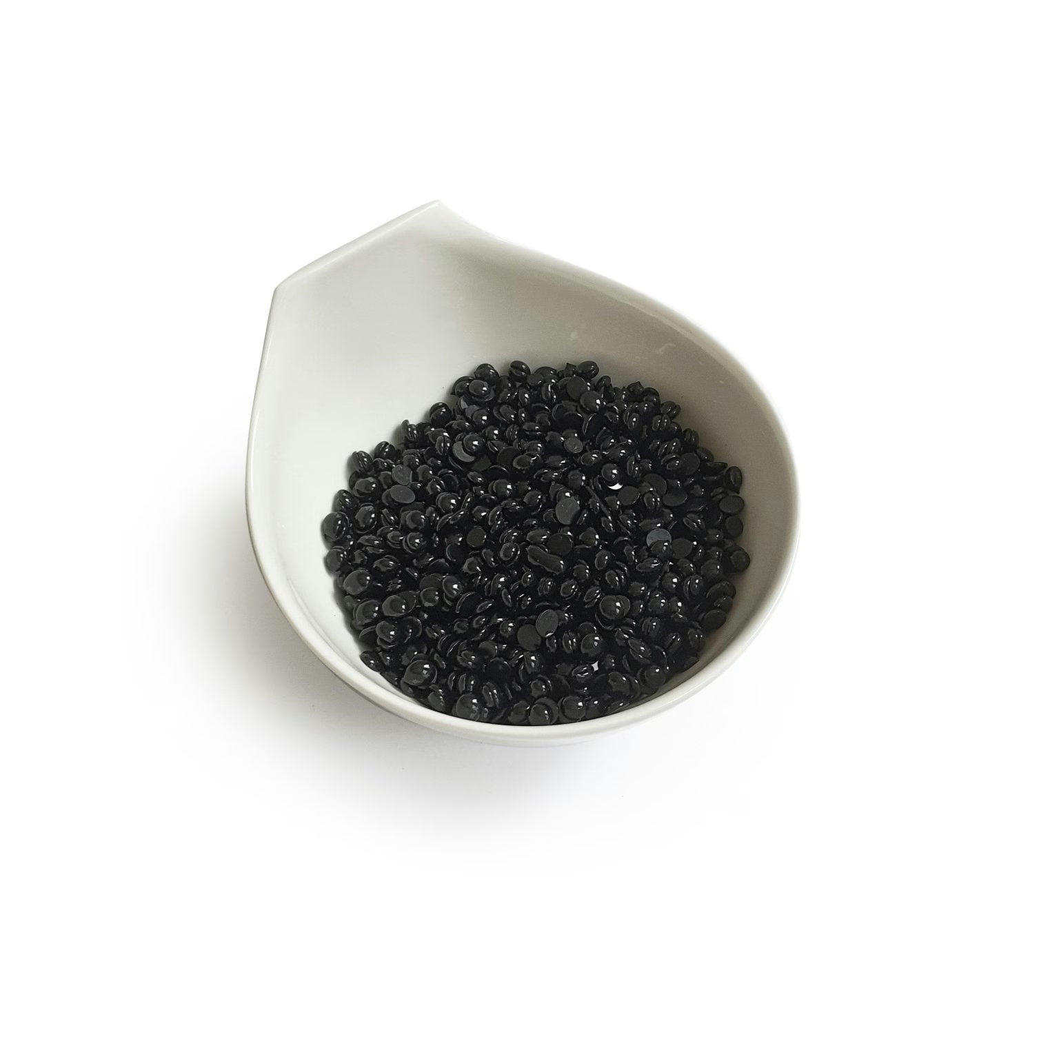 Black Coral Hard Wax  by Black Coral Wax USA is showcased in a white ceramic bowl akin to a Black Coral Hard Wax vessel. The bowls subtle, spout-like design elegantly cradles small, shiny black beads against a plain backdrop, reflecting potential for long-lasting hair removal.
