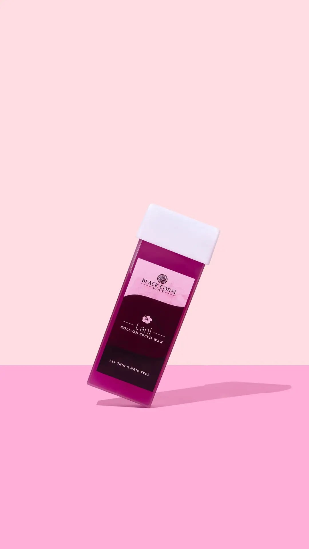 A pink and maroon Lani Roll-On SpeedWax cartridge by Black Coral Wax USA stands upright on a pink background with a shadow. The label states it suits all skin and hair types.