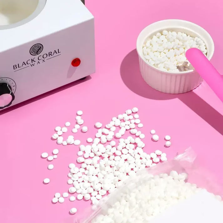 White wax pellets with a waxing machine and container on a pink background